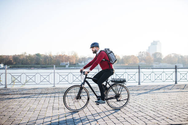 Hipster businessman commuter with electric bicycle traveling to work in city. A side view of hipster businessman commuter with electric bicycle traveling to work in city. Copy space. energy fuel and power generation city urban scene stock pictures, royalty-free photos & images