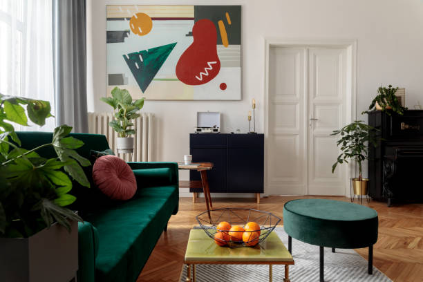 istock Luxury home interior with design velvet sofa, coffee tables, pouf, commode and accessroies. A lot of plants on the piano. White walls with painting. Sunny view. Stylish decor of sitting room. 1125385991