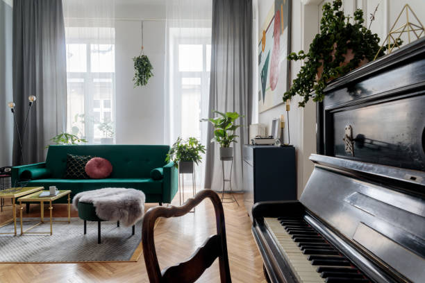 istock Bright and sunny luxury home interior with design green velvet sofa, armchair, table, commode, pouf and accessroies. Big windows. A lot of plants. Stylish decor of living room. View from the piano. 1125386078