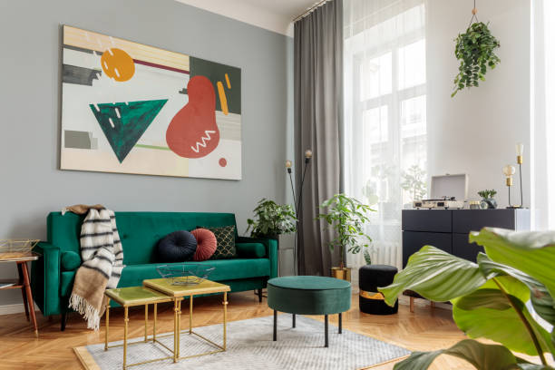 istock Luxury and modern home interior with design green sofa, commode, coffee tables, pouf and accessroies. A lot of plants in the room. Abstract painting. Stylish decor of living room with brown parquet. 1125386141