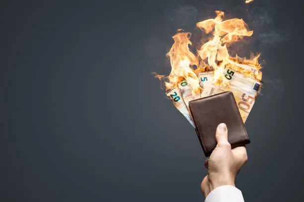 Euro bills are burning with bright flames. They are held in a wallet by one hand.