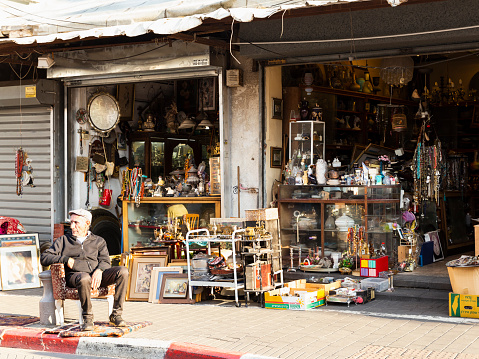 Old Jaffa, Tel Aviv, Israel - December 23, 2018: A old vendor sitting in armchair in front of his antique shop in famous flea market in Old Jaffa, Tel Aviv, Israel.
