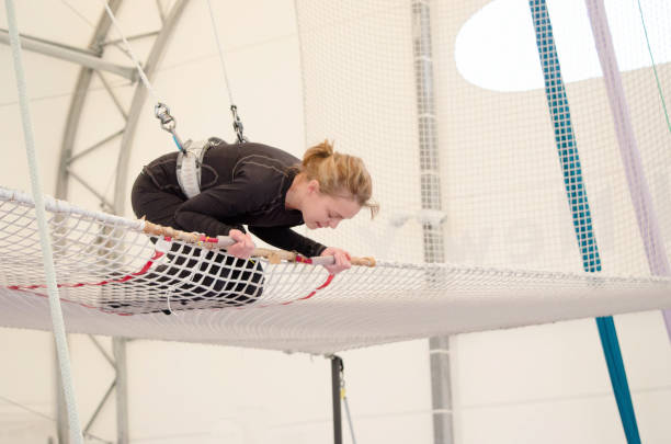 An adult female lands on a net, preparing to dismount at a on a flying trapeze school at an indoor gym. The woman is an amateur trapeze artist. An adult female lands on a net, preparing to dismount at a on a flying trapeze school at an indoor gym. The woman is an amateur trapeze artist. safety net stock pictures, royalty-free photos & images