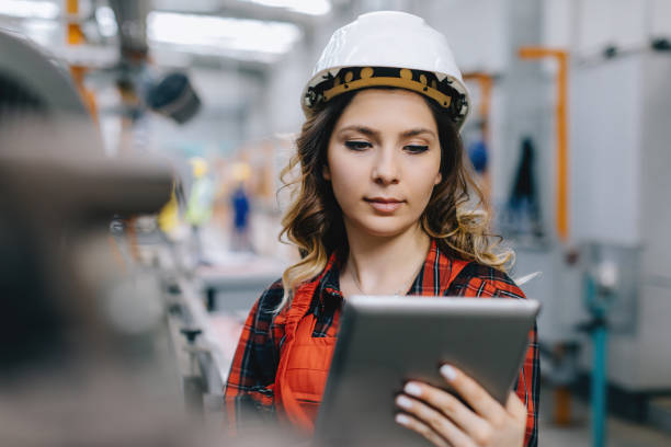 Young female maintenance engineer working with digital tablet Woman in protective clothing in factoryYoung electrical engineer woman using touchpad with digital tablet and standing in front of control panel  working about technical problems and writes the results of measurements in control room of modern thermal or nuclear power plant electric energy station. drawing board stock pictures, royalty-free photos & images