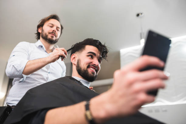 istock Men in a Barber Shop Using Smart Phone While Having Haircut 1125423035