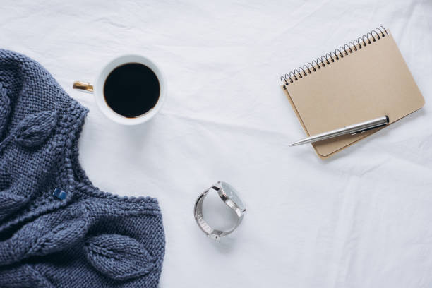 istock Cup coffee , blue knitted sweater, notebook with pen, clock on bed, top view. 1125423485