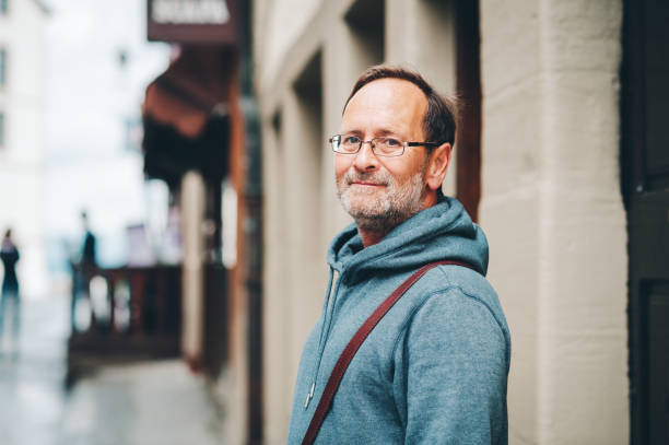 outdoor portret van 50-jarige man dragen hoody blauw en brillen - europese etniciteit stockfoto's en -beelden