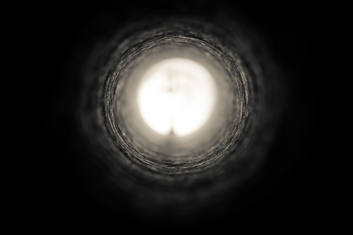 View looking down a long cardboard mailing tube towards the a source of bright light in the distance.  Selective focus, focused mid-distance.  Toned imaged.   Belfast, Northern Ireland.