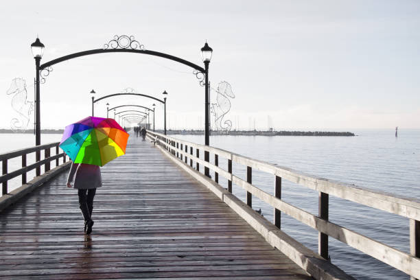 woman holding a rainbow colored umbrella walking on a rainy day. - sex district imagens e fotografias de stock