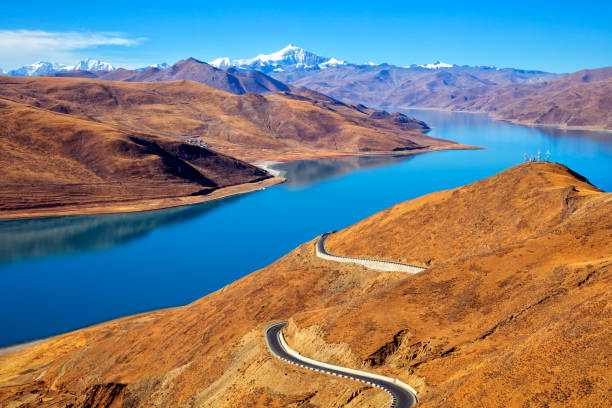 Yamdrok Lake at a height of 4900 m, mountain range and winding road  in Himalaya, Tibet. In the background is seen Noijinkangsang peak (7206 m). Yamdrok Lake is situated about 100 km from Lhasa, the capital of Tibet.