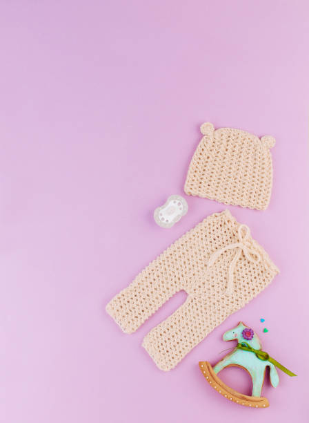 Small knitted hat and pants for newborn baby on violet background