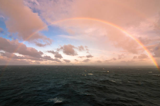 rainbow in the middle of the sea with a beautiful blue sky full of clouds