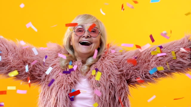 Cheerful senior woman stylish fur enjoying falling confetti, festival happiness