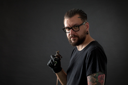 Studio portrait of tattoo artist with tattoo machine on black background
