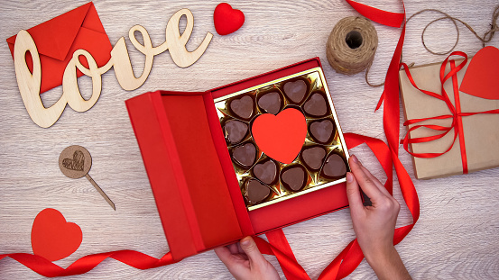 Lady opening Valentines giftbox with heart-shaped chocolate candies, aphrodisiac