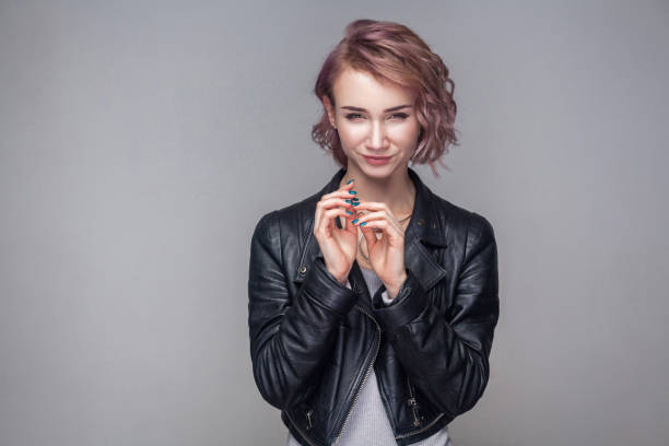 Portrait of cheater beautiful girl with short hairstyle, makeup in casual style black leather jacket standing with cunning idea and looking at camera Portrait of cheater beautiful girl with short hairstyle, makeup in casual style black leather jacket standing with cunning idea and looking at camera. indoor studio shot, isolated on grey background. revenge stock pictures, royalty-free photos & images