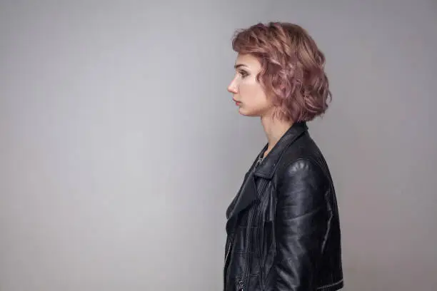 Photo of Profile side view portrait of serious beautiful girl with short hairstyle and makeup in casual style black leather jacket standing and looking aside