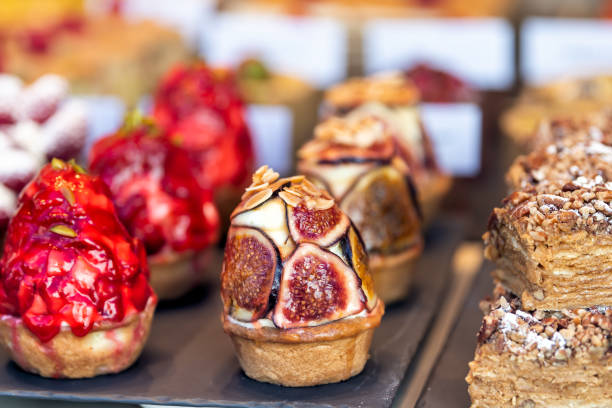 Display of many tarts cupcakes stuffed with cream desserts on trays in gourmet bakery cafe pastries closeup with fruit figs and strawberries