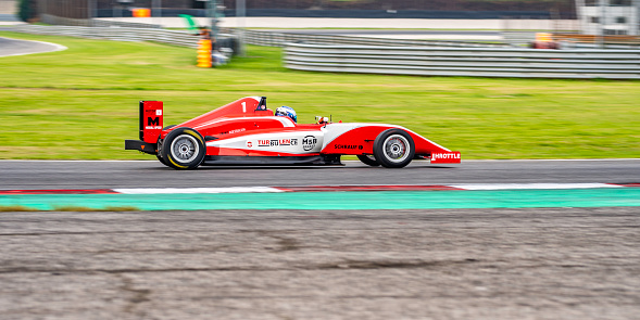 Side view panning shot of a red open-wheel single-seater racing car race car speeding on the track.