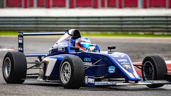 Close-up of a race car driver in a formula car driving fast on the track.