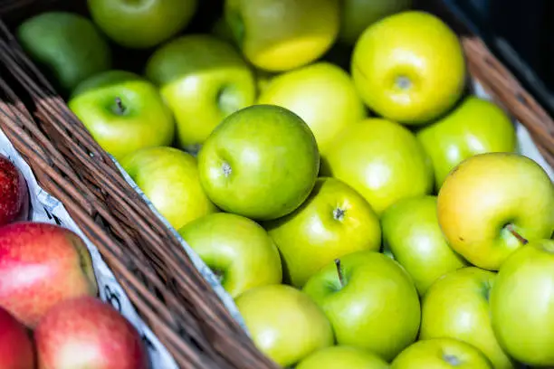 Closeup of many granny smith green yellow apples in basket at farmer's market shop store showing detail and texture assortment