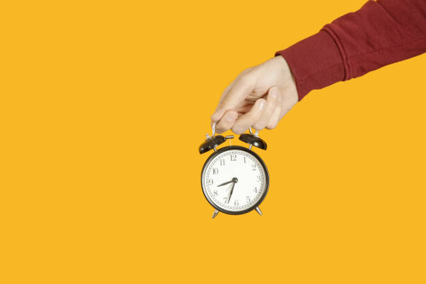 istock Man holding black alarm clock against a yellow background 1125471911