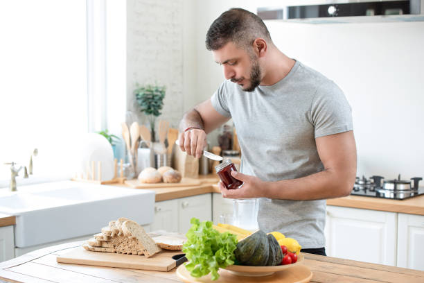 Male caucasian preparing breakfast in a kitchen Mature fit bearded caucasian man preparing healthy breakfast sandwich in kitchen making a sandwich stock pictures, royalty-free photos & images