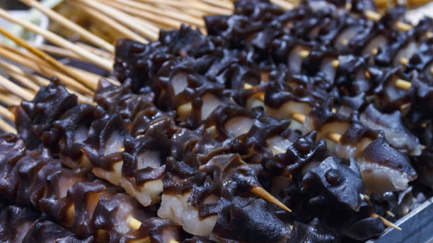 Fast food in the Asian market. Snack on wooden chopsticks resembles a sea cucumber prepared for frying Fast food in the Asian market. Snack on wooden chopsticks resembles a sea cucumber prepared for frying A popular snack for tourists. holothuria stock pictures, royalty-free photos & images