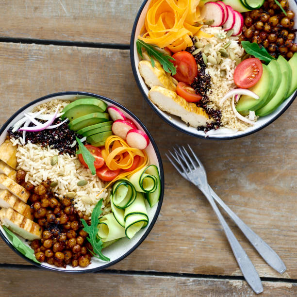 Two buddha bowl. Clean and balanced healthy food concept. Chicken grilled steak, rice, spicy chickpeas, black and white quinoa, avocado, carrot, zucchini, radish, tomatoes on wooden table top view