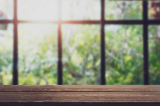Wooden board empty table in front of blurred window view in the garden.