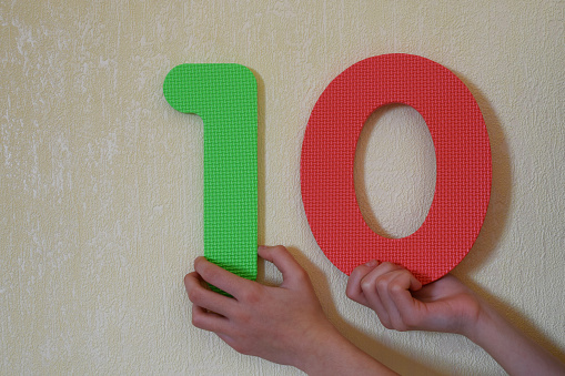 10 - hands holding colorful number one and zero or ten on mild yellow wall background with copy space for text. 10th anniversary or birthday design.