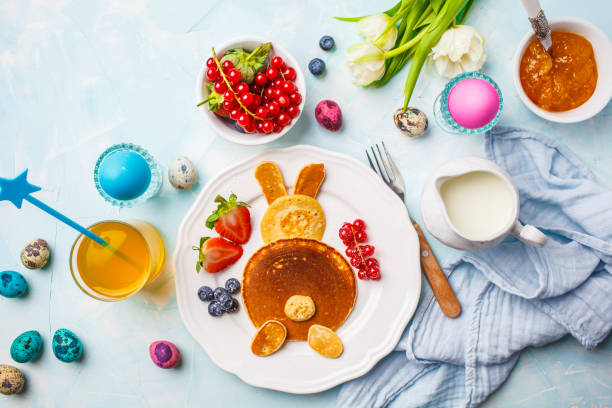 Easter bunny of pancakes with berries. Easter Breakfast table. Blue background, top view. Easter bunny of pancakes with berries. Easter Breakfast table. Colored eggs, milk, juice and jam. Blue background, top view. bunny pancake stock pictures, royalty-free photos & images