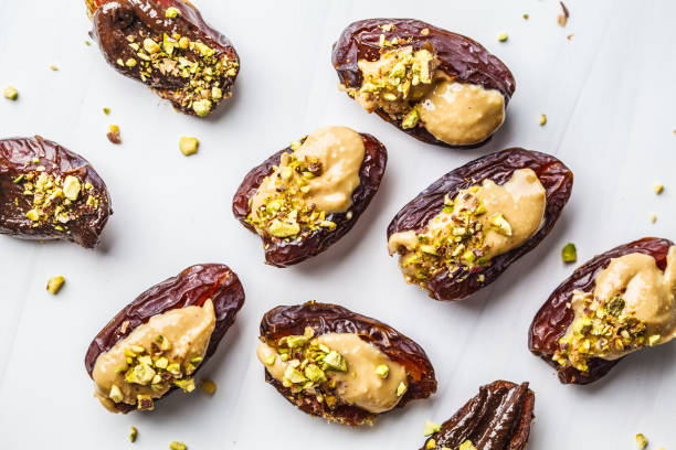 Dates stuffed with peanut butter and pistachios on white background.