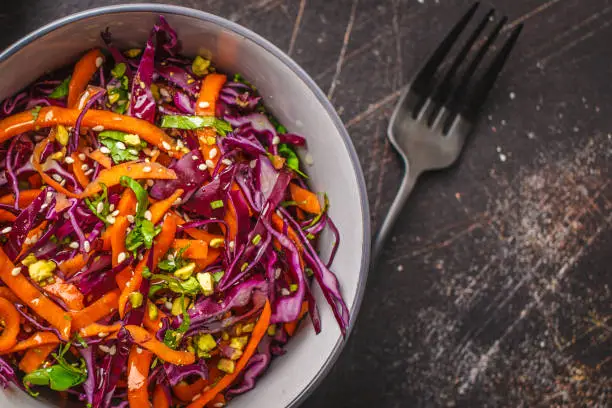 Coleslaw salad in a gray bowl on a dark background. Red cabbage and carrot salad.