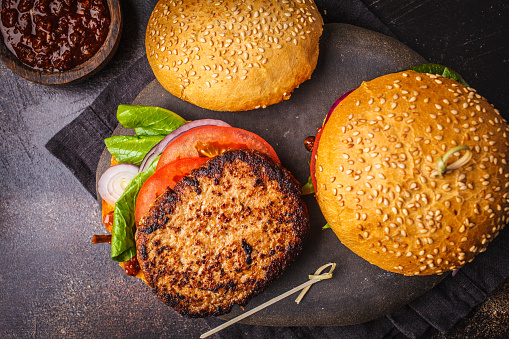 Homemade open burgers with meat and vegetables on a dark background.