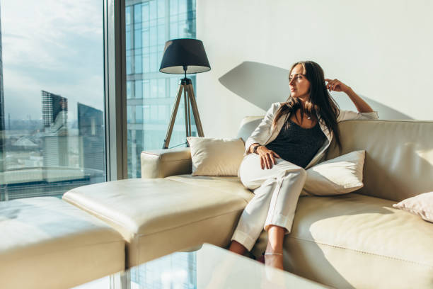retrato de mulher de negócios bem sucedido usando elegante terno formal sentado no sofá de couro relaxando depois do trabalho em casa - relaxation success luxury women - fotografias e filmes do acervo