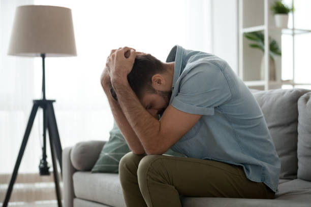 istock Depressed sad man sitting on couch holding head in hands 1125572476