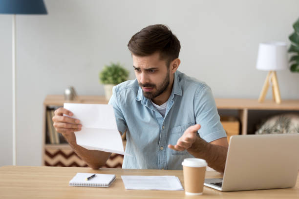 confused frustrated man holding mail letter reading shocking unexpected news - declaring bankrupcy imagens e fotografias de stock