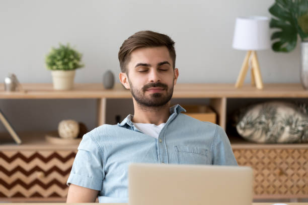 Happy relaxed young man resting with eyes closed breathing air Happy relaxed young man resting with eyes closed breathing fresh air in dreamy mood at work desk, healthy calm guy lounge at home enjoy peaceful break feeling peace of mind stress free relief concept meditation room office stock pictures, royalty-free photos & images