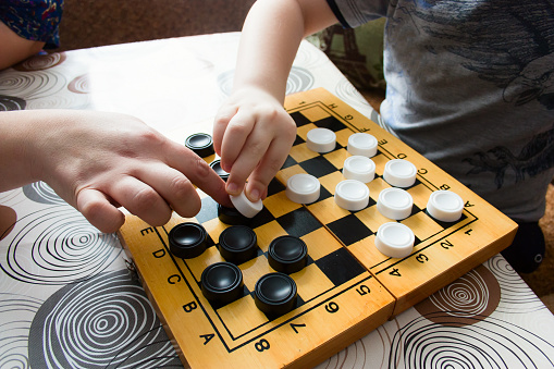 unrecognizable  woman and kid playing checkers at home,  closeup of a child's hand and mother's hand  moves figures