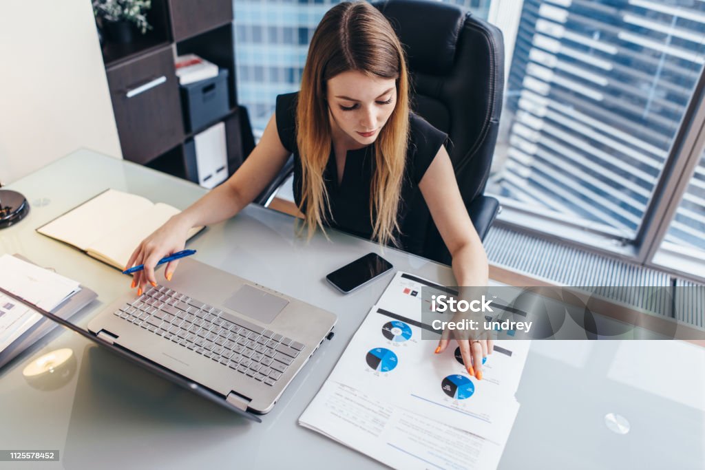 Female businesswoman readind financial report analyzing statistics pointing at pie chart working at her desk Female businesswoman readind financial report analyzing statistics pointing at pie chart working at her desk. Finance Stock Photo Female businesswoman readind financial report analyzing statistics pointing at pie chart working at her desk Female businesswoman readind financial report analyzing statistics pointing at pie chart working at her desk. Finance Stock Photo