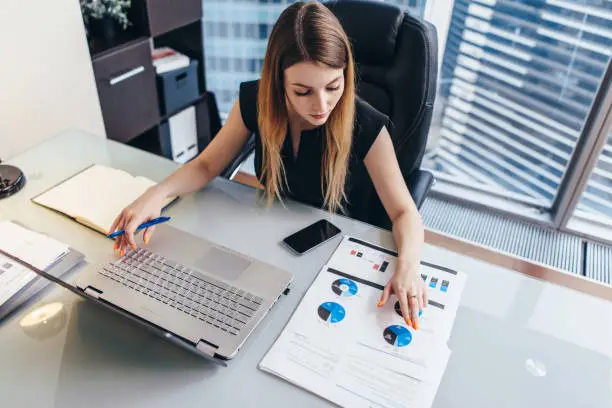 Photo of Female businesswoman readind financial report analyzing statistics pointing at pie chart working at her desk