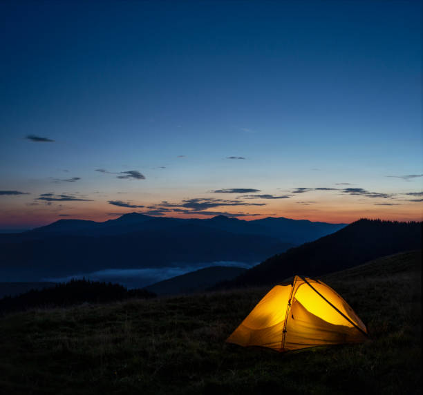 istock Orange lighted tent in mountains under evening sky 1125589054