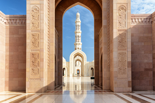 Amazing view of minaret through scenic arches of the Sultan Qaboos Grand Mosque in Muscat, Oman. Beautiful Islamic architecture. The Muslim place is a popular tourist attraction of the Middle East.