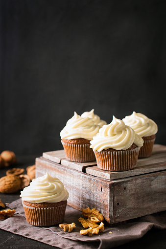 Carrot cupcakes or muffins with nuts on dark background, copy space, vertical