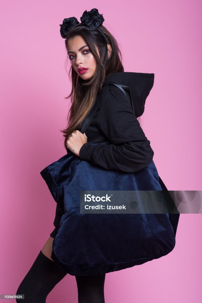 Beautiful asian young woman in black clothes against pink background Studio portrait of young woman wearing black hooded shirt, knee socks and headband, standing against pink background. Bag Stock Photo