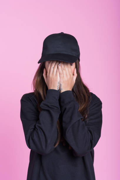 молодая женщина в черной одежде, закрываюющая лицо в руках - black cap стоковые фото и изображения