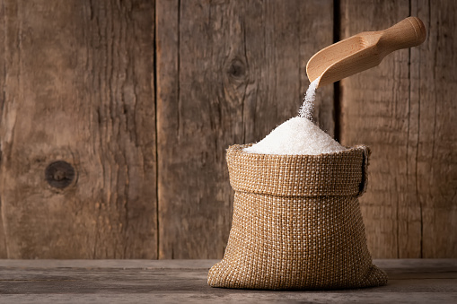 white sugar sand falling in sack on wooden background