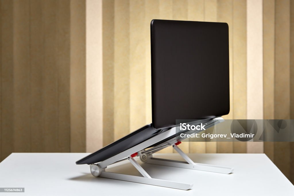 The laptop is open and mounted on a cooling stand. Adjustable portable aluminum laptop  holder folding with open pc notebook, back view. Laptop Stock Photo
