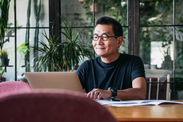 sorridente homem chinês trabalhando no laptop em casa - asian ethnicity computer business chinese ethnicity - fotografias e filmes do acervo